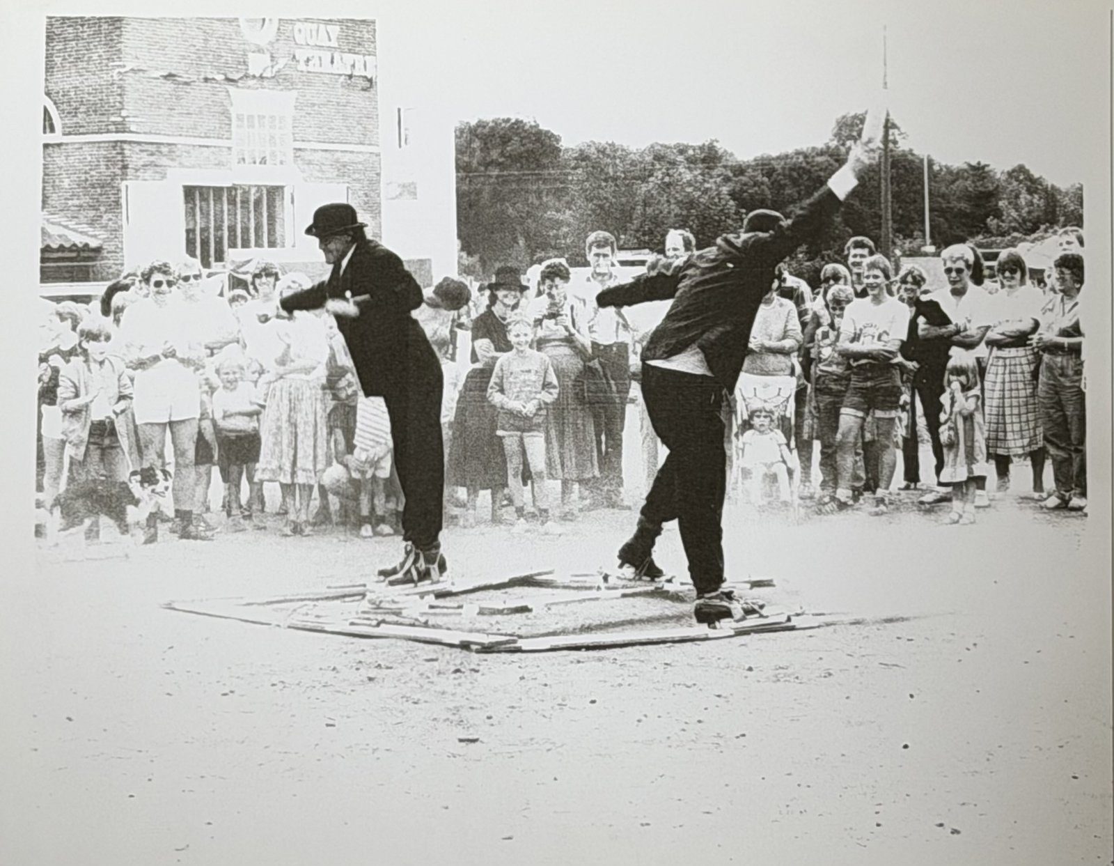 Walkwork in performance — figures bound to shared timber skis, moving together before a crowd